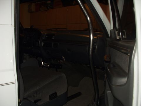 1993 Ford Bronco - The interior of a vehicle is visible, a roll cage and fabric seats, with the dashboard and door panel also in view.