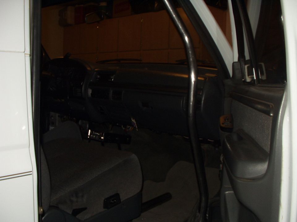 Gray vehicle interior with dash trim removed exposing wiring, bench seat and open door
