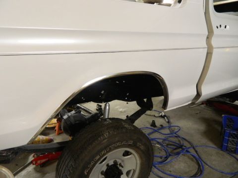 1979 Ford Bronco - The rear passenger side of a white pickup truck is shown, with the wheel removed and suspension components visible.