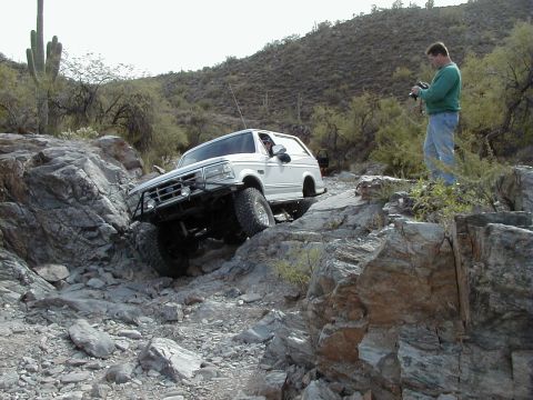 1993 Ford Bronco - White 1993 Ford Bronco tackles a challenging rocky off-road path in a desert environment.