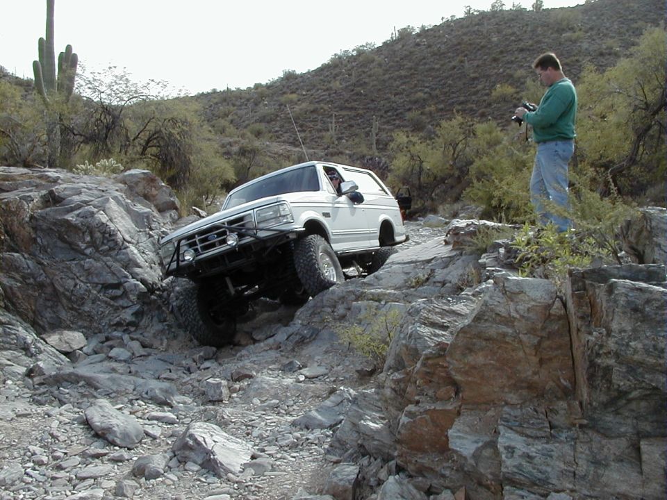 White lifted Ford Bronco crawling down a rocky desert ledge with tube bumper
