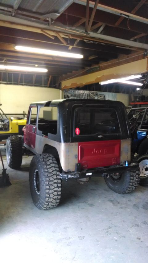 1985 Jeep CJ7 - This Jeep CJ-series is in a garage, showing its rear with large off-road tires and a red tailgate.
