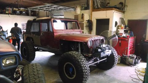 1985 Jeep CJ7 - A modified Jeep CJ-series is parked in a workshop, with another vehicle partially visible in the foreground.