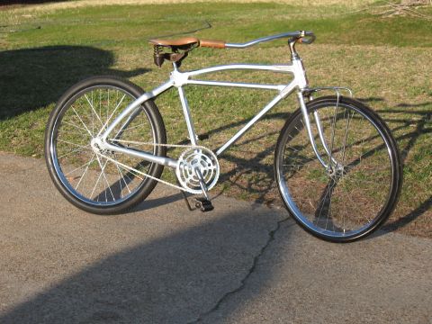 Silver custom bicycle with a brown leather seat and wooden handlebars, viewed from the side