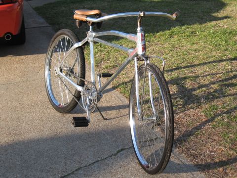 Chrome bicycle front view with brown leather seat and red/white badge on frame