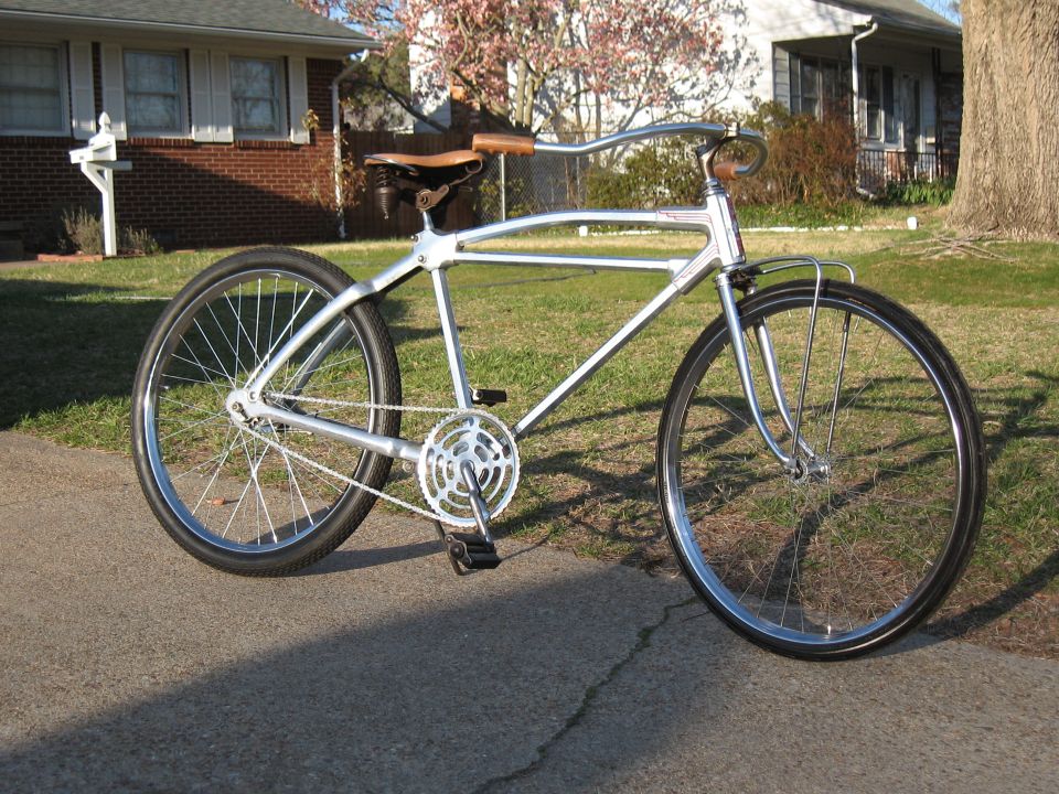 Silver custom bicycle with leather seat and handlebars, parked on a driveway