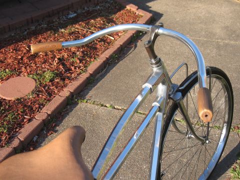 Chrome bicycle handlebars with wooden grips, front wheel, and part of frame