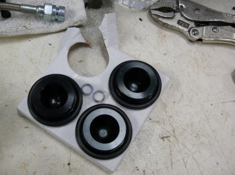 Three black rubber seals and two metal rings on a white cardboard insert, with a vise grip and braided hose in