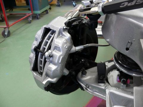 Close-up of a silver brake caliper over a vented rotor, with suspension components visible