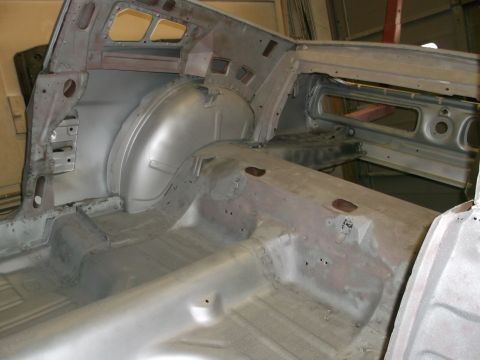 1967 Ford Mustang - The interior of a car stripped down to bare metal reveals the floor pan and rear wheel wells, indicating a restoration project.