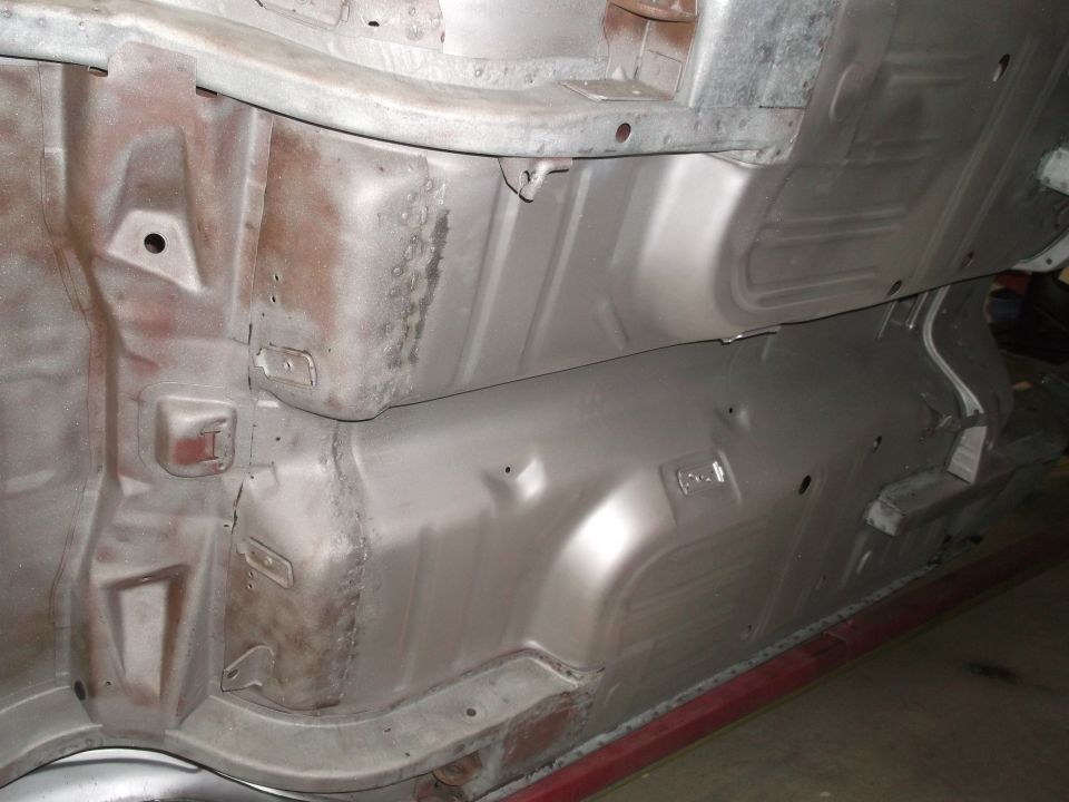 Underside of a car showing floor pans and frame rails, some rust visible