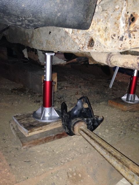 1991 Ford Bronco - The underside of a vehicle is raised on jack stands, showing rusty frame components and exhaust pipes.