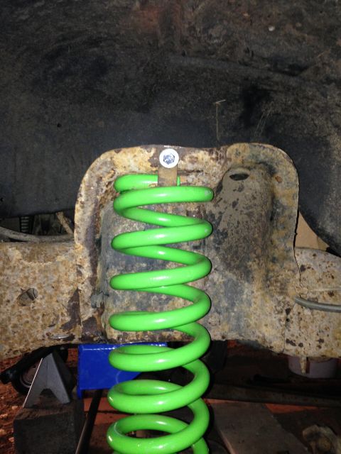 1991 Ford Bronco - A bright green suspension spring is visible, mounted on a rusty vehicle frame, supported by a blue jack stand.