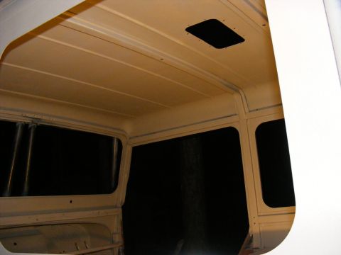 Interior of a vehicle with tan headliner and blacked-out windows, showing a roof vent