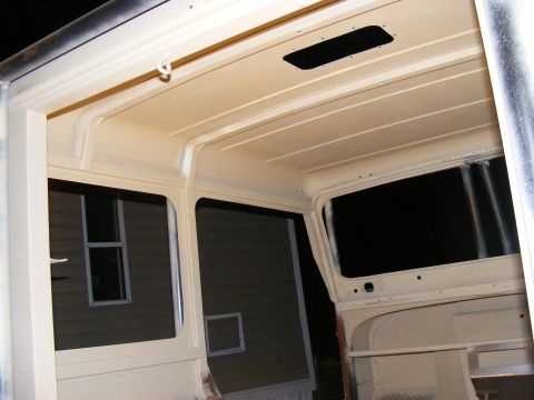 Interior view of a vehicle with cream-colored headliner and windows, showing construction