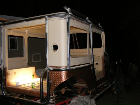Custom off-road vehicle body with roll cage and diamond plate fender, under construction at night