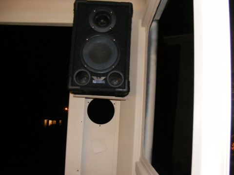 speaker mounted on a white panel, with a dark background outside