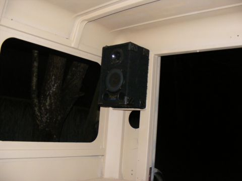 Interior view of a vehicle with a black speaker mounted on a cream-colored pillar near a window
