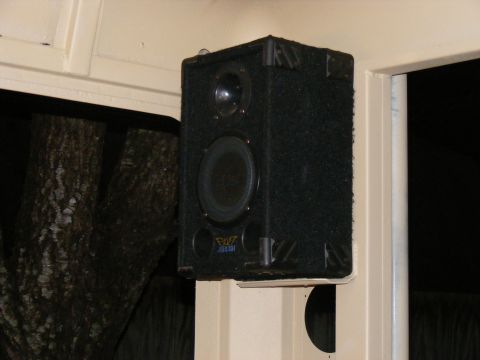 Black car speaker with a yellow logo and blue text mounted on a cream-colored interior panel