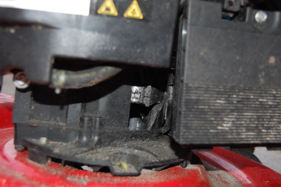 Close-up of a lawn mower engine component with a hose and warning symbols