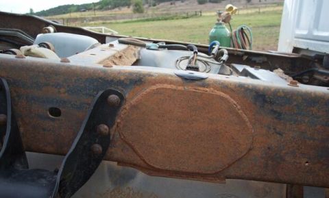1990 Ford Bronco - Close-up of a heavily rusted truck frame, showing fuel tank and lines, with welding equipment in the background.