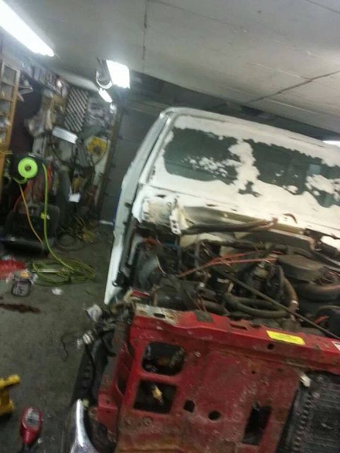 1995 Ford F-150 - A truck is in a garage, undergoing repairs with its engine exposed and front body panels removed.
