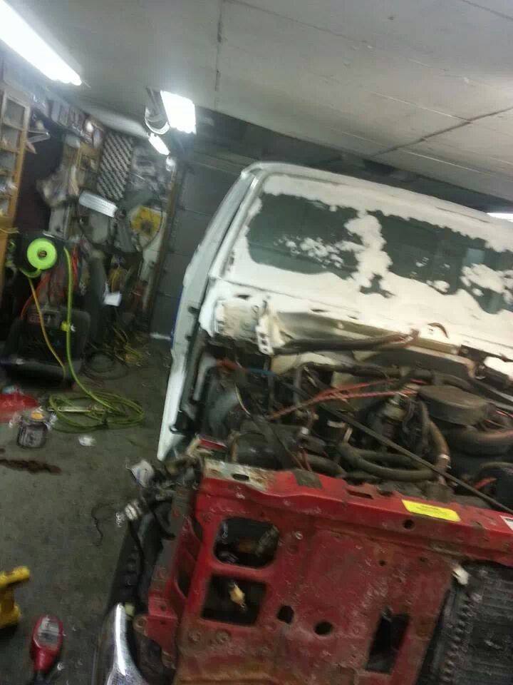 Truck in a garage with the hood open and front end disassembled. Looks like it's being worked on