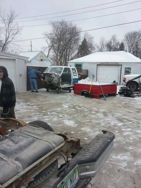 1995 Ford F-150 - Disassembled truck parts are scattered around a snowy driveway with garages in the background.