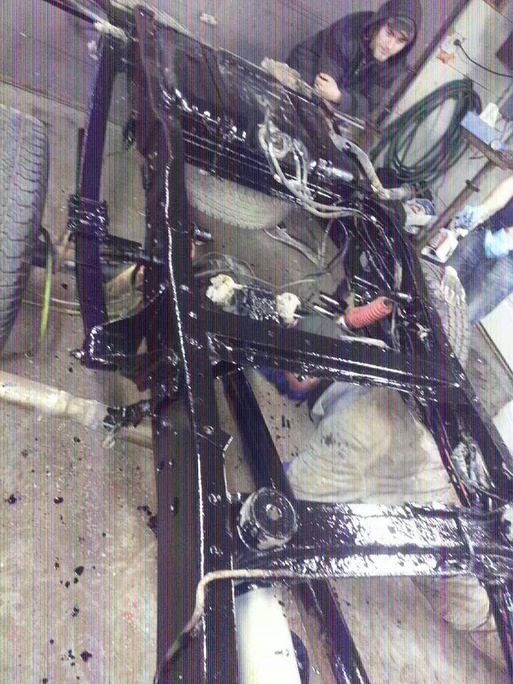 Black painted vehicle frame with suspension components visible, two people working on it