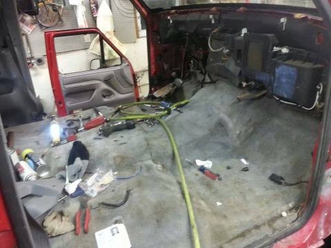 1995 Ford F-150 - The interior of a red 1995 Ford F-150 is shown with its dashboard disassembled and carpet removed, revealing tools and wiring.