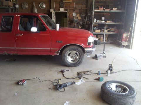 1995 Ford F-150 - A red 1995 Ford F-150 truck is parked in a garage, surrounded by various tools and a spare tire, suggesting ongoing maintenance or repair.