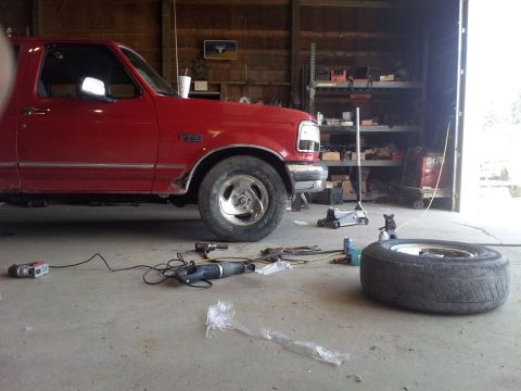 1995 Ford F-150 - Red 1995 Ford F-150 truck in a garage, undergoing tire maintenance with tools and a spare tire nearby.