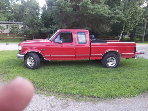 1995 Ford F-150 - A red 1995 Ford F-150 pickup truck is parked on a grassy area with trees in the background.