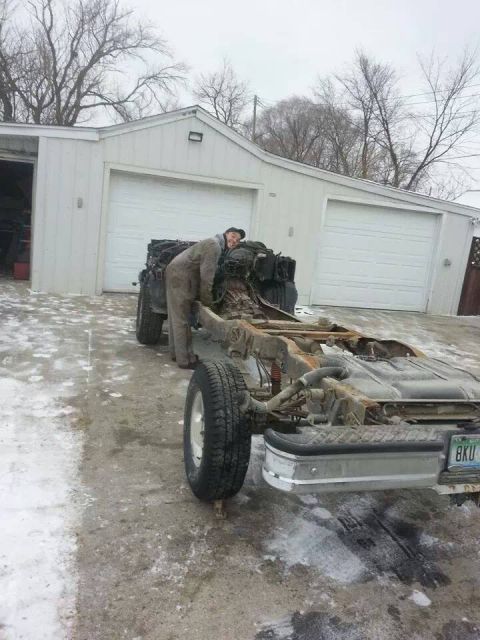 1995 Ford F-150 - A person works on the engine of a 1995 Ford F-150 chassis outside a garage.