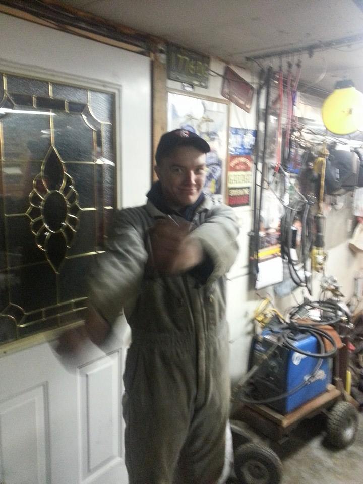 Man in overalls stands in a cluttered garage, arms crossed