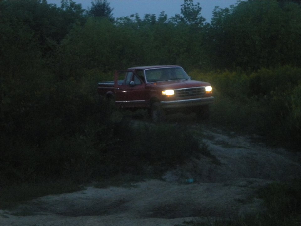 Red pickup truck driving on a dirt path at dusk, headlights on