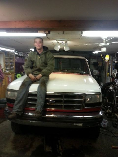 1995 Ford F-150 - Man sits on the hood of a white 1995 Ford F-150 truck in a garage setting.