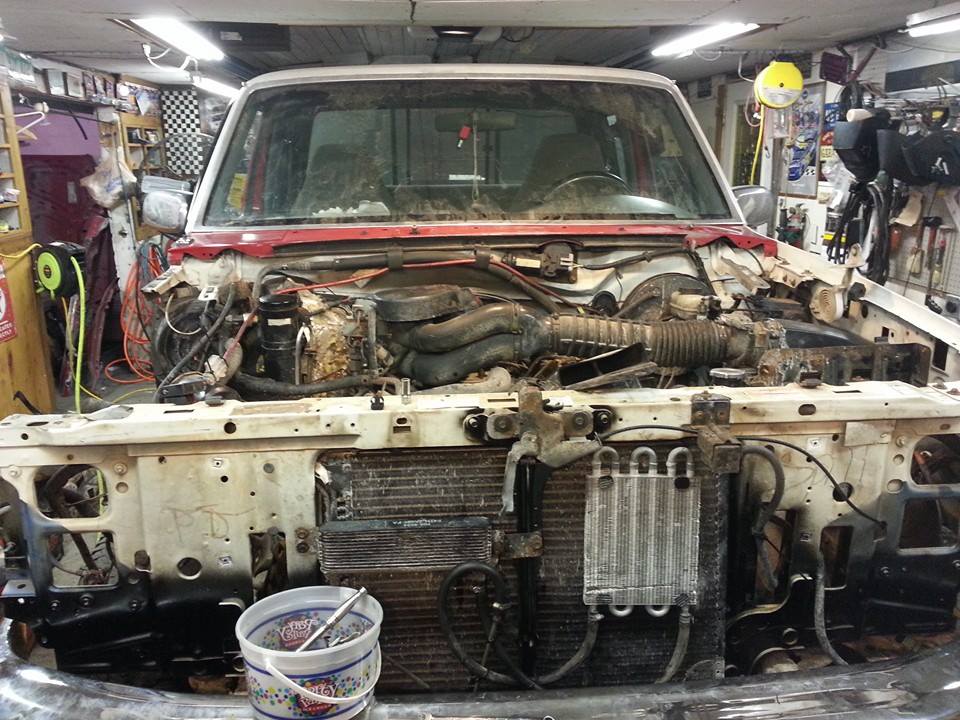 Truck front end with hood removed, showing engine and radiator components. Tools in a bucket are visible