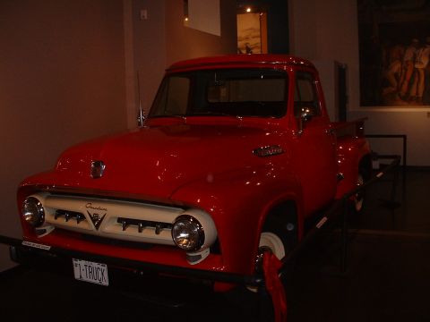 1999 Ford Crown Victoria - A bright red 1956 Ford F-100 pickup truck is displayed indoors, a prominent white grille and a custom license plate.