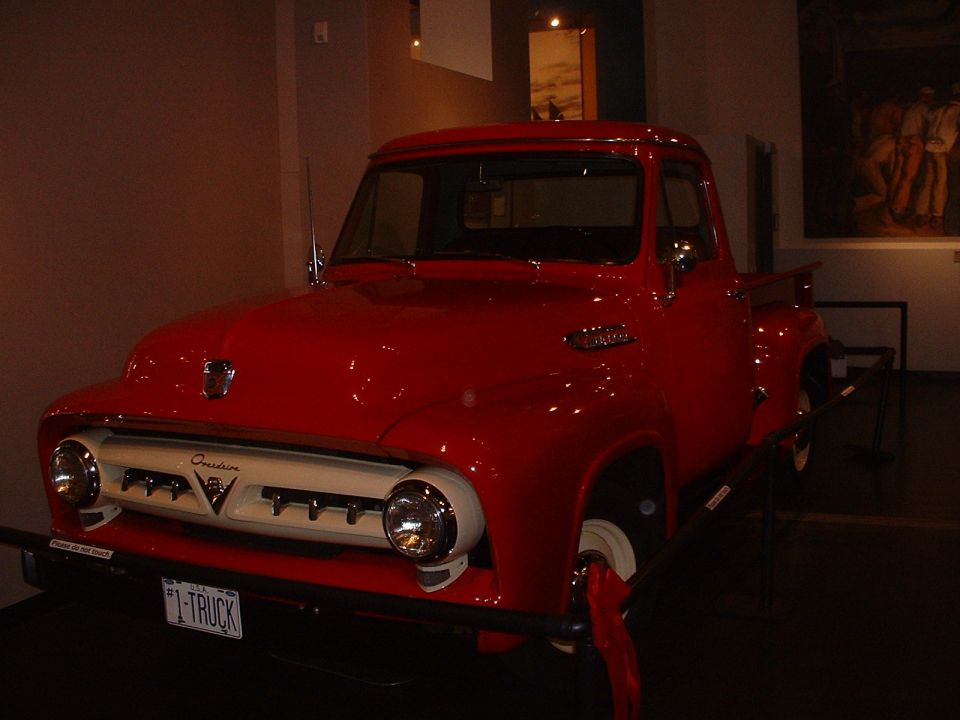 Red 1956 Ford F-100 pickup truck with a white grille and "I-TRUCK" license plate