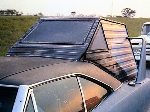 1972 Ford Ranchero - A unique camper shell is mounted on the rear of a car, with another vehicle partially visible in the background.
