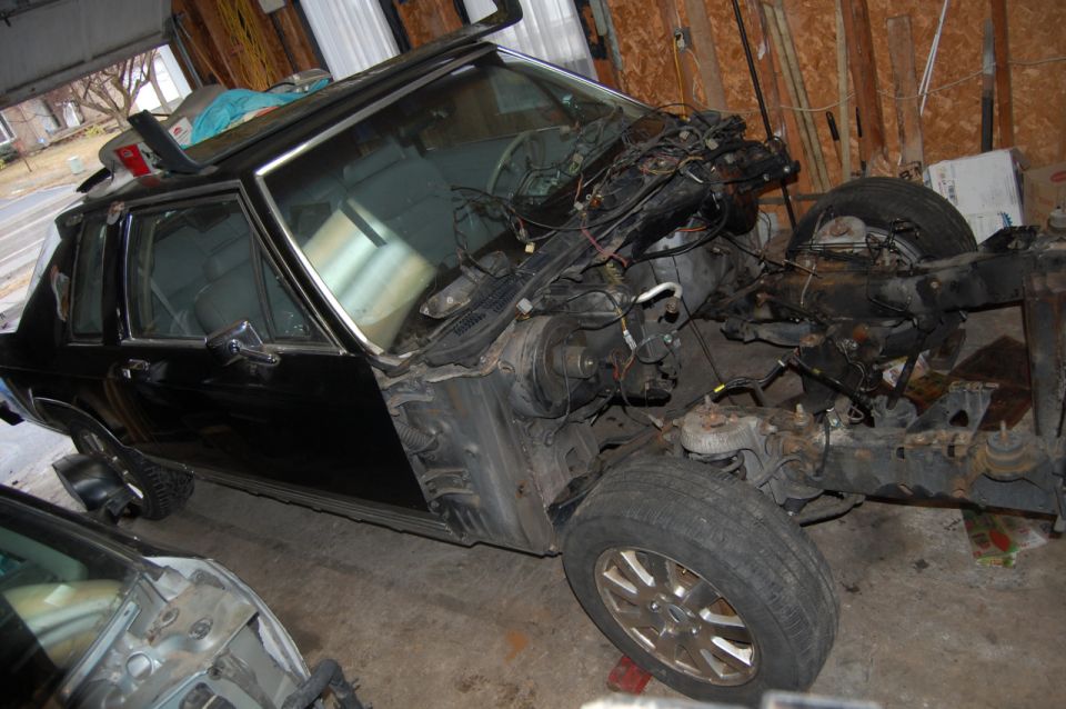 Black SUV or truck with front clip removed during disassembly in a garage