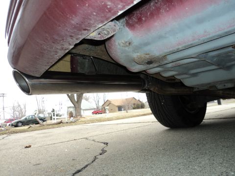 2004 Mercury Grand Marquis - A close-up shot of a car's exhaust system and tire, with a residential street scene in the background.