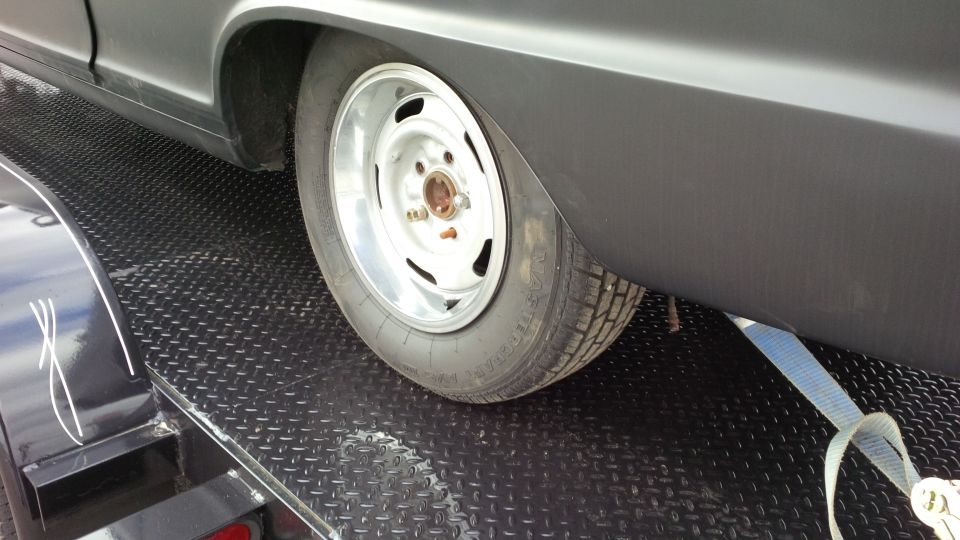 Gray car fender and chrome wheel with tire on a black diamond plate trailer, secured with a blue strap