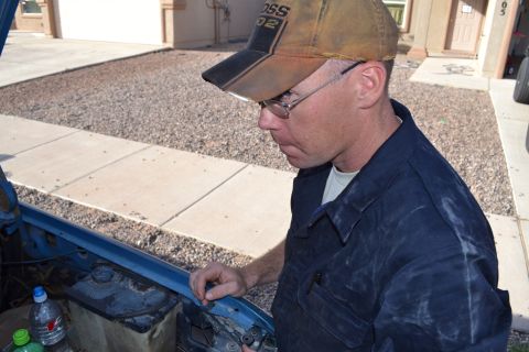 1981 Ford F-250 - Man inspects the engine bay of a blue vehicle, wearing a 'BOSS 02' hat.