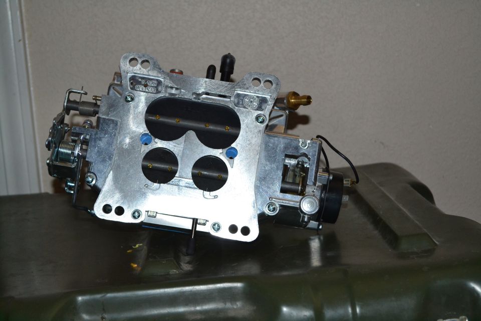 Aluminum carburetor with four black circular openings, resting on a dark green surface