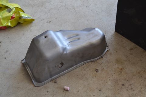 1981 Ford F-250 - A metal oil pan rests on a concrete surface, with a yellow bag and a black object in the background.