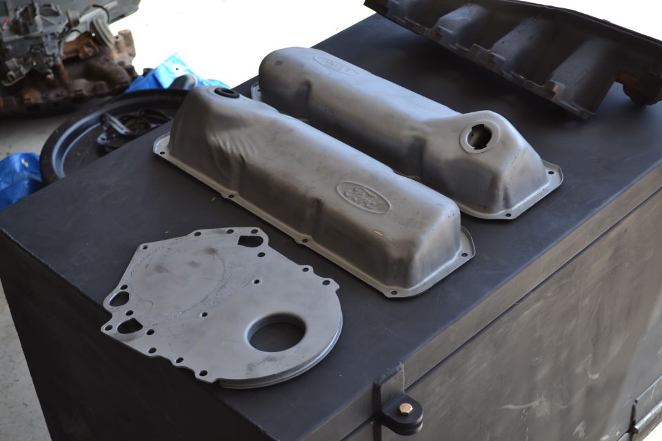 Two Ford valve covers and a timing cover on a black surface. Supermotors.net logo visible