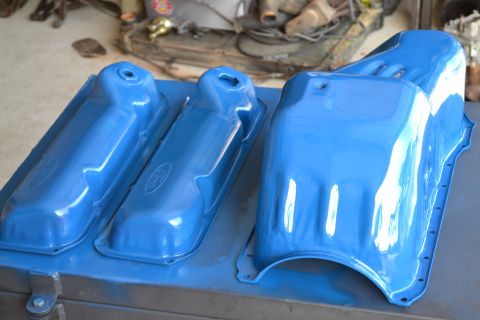 1981 Ford F-250 - Freshly painted blue engine parts, including valve covers and an oil pan, are laid out on a workbench.
