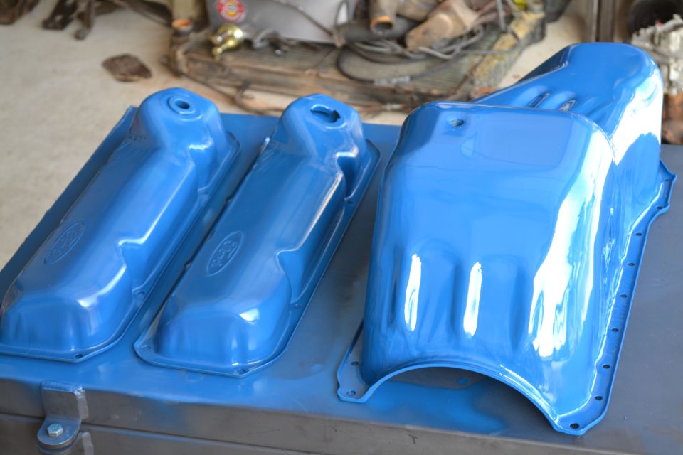 three blue painted Ford valve covers and an oil pan on a workbench
